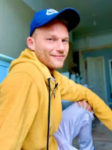 Daniel Harris at home wearing a yellow top and blue baseball cap smiling